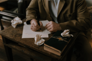 Writer jotting on a piece of paper at a brown desk.