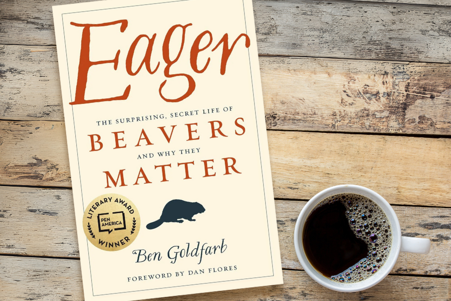 A copy of the book "EAGER" beside a cup of black coffee on a wooden tabletop