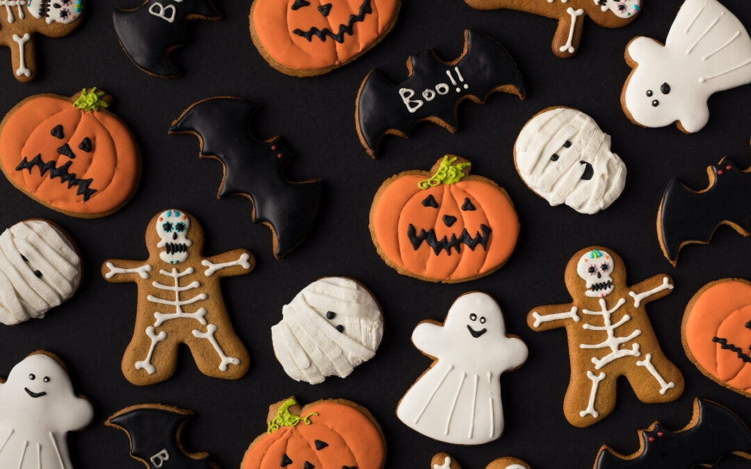 Cookies decorated to look like ghosts, pumpkins, bats, and mummies atop a black background