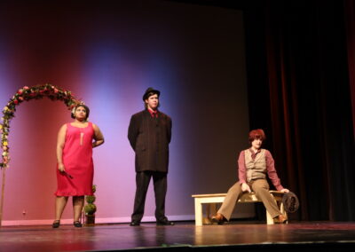 A female and male actor talking to an actor on a bench