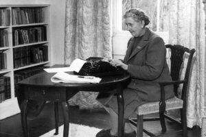 Black and white image of author Agatha Christie sitting at a typewriter